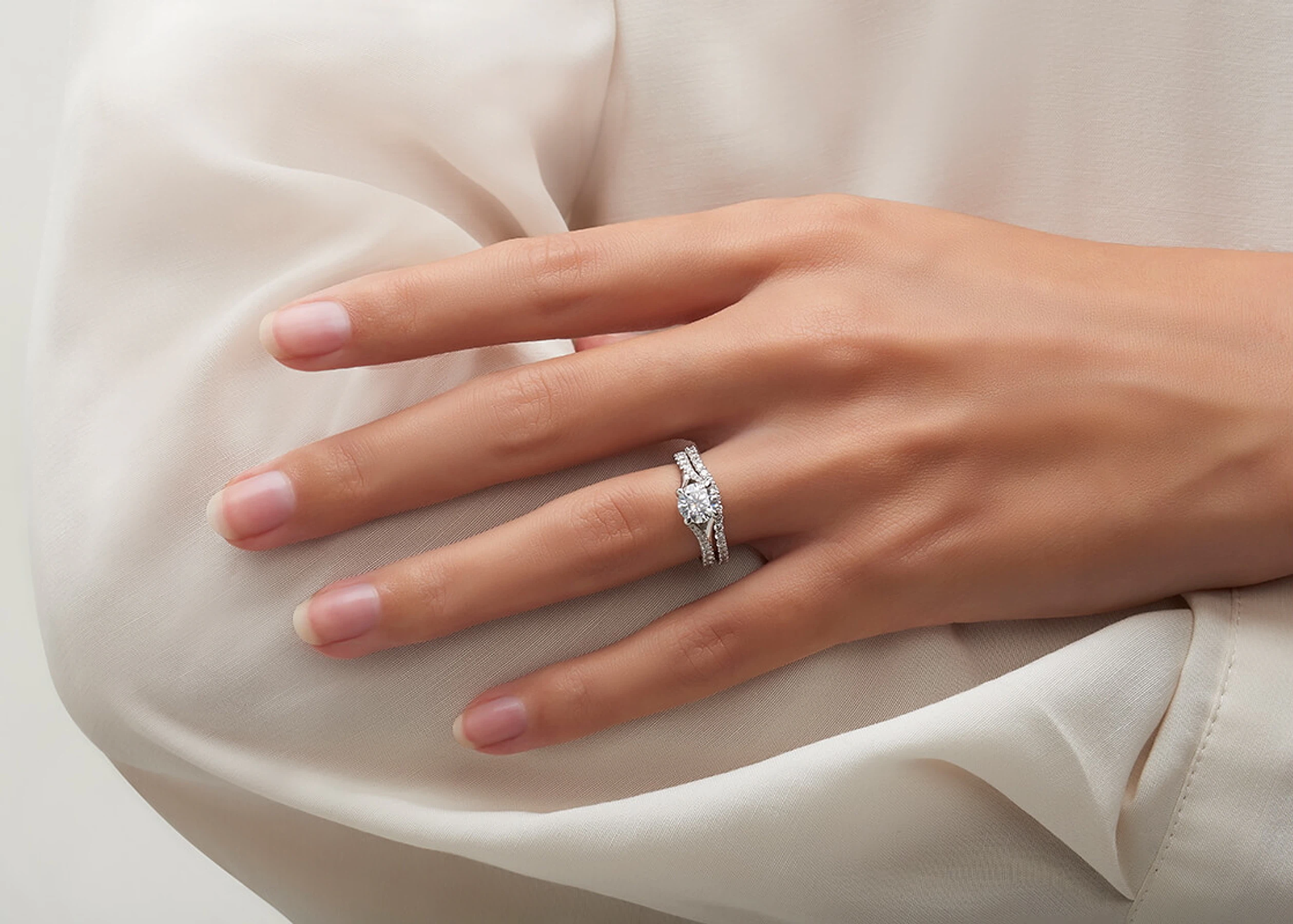 El anillo Violetta y la argolla Encuentro juntos en una mano, en oro blanco, sobre tela marfil
